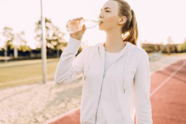 Atletik güzel koşucu koştuktan sonra plastik şişeden su içer. Bir kız açık hava fitness derslerinden sonra susuzluğunu giderir.