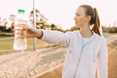 Stadyumun dışında elinde su şişesiyle duran güzel atletik bayan koşucu. Spor yaparken spor yapan kadın ara verir.