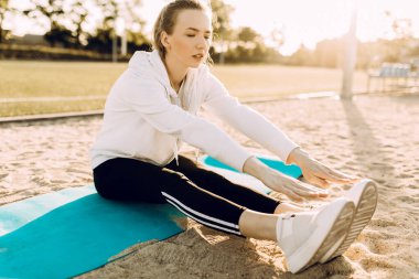 Güzel bir atletik kadın temiz havada koştuktan sonra geriliyor. Güneşli bir günde, bir sporcu bir parkta ya da ormanda bir fitness minderinde gerilir..