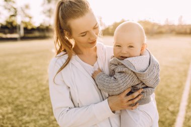 Mutlu genç anne, küçük çocuğunu kollarına alıp gün batımında dışarıda kucaklıyor.