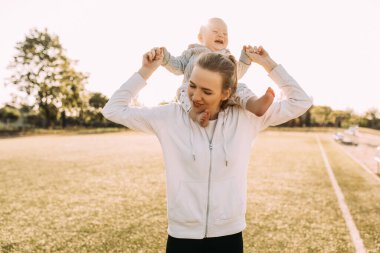 Genç bir kadın gün batımının arka planında genç oğlunu boynunda tutuyor. Anne ve küçük oğlu doğada iyi vakit geçiriyorlar. Anneler Günü. Aile kavramı