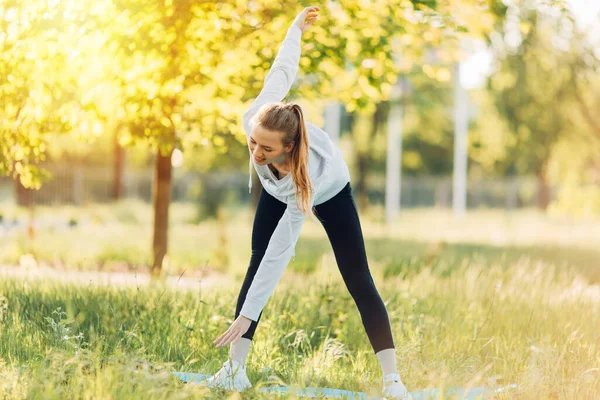 Athletic young woman doing sports in the Park in the morning, women's workout on a yoga Mat