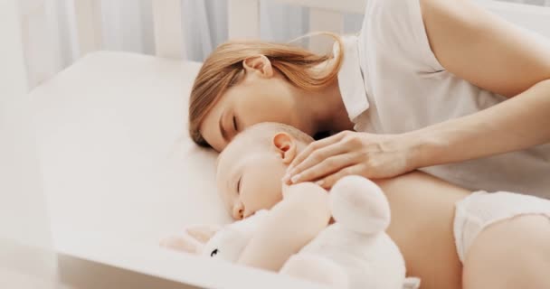 Vista laterale di una bella giovane madre e del suo piccolo bambino carino che dorme a letto a casa — Video Stock