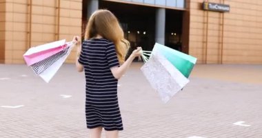 Alışveriş merkezinin arka planında alışveriş çantaları olan mutlu, güzel bir kız.