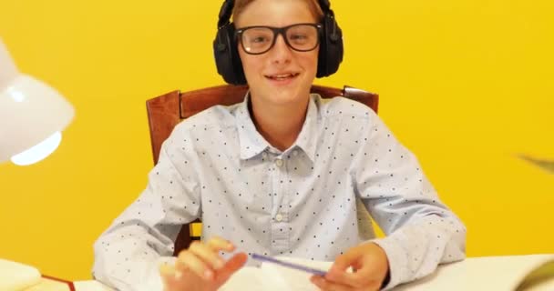 Щасливий хлопець-підліток в навушниках, використовуючи ноутбук, навчається через онлайн систему електронного навчання, на жовтому фоні — стокове відео