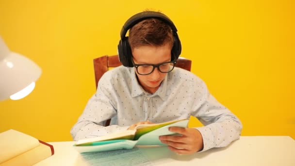 Écolier adolescent guy dans casque, lecture d'un livre d'apprentissage à travers un e-learning système en ligne, sur un fond jaune quarantaine, coronavirus, pandémie — Video
