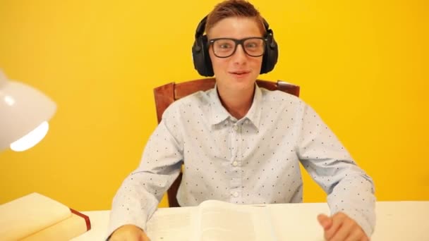 Happy teen guy in headphones using a laptop computer, learning through an online e-learning system, on a yellow background