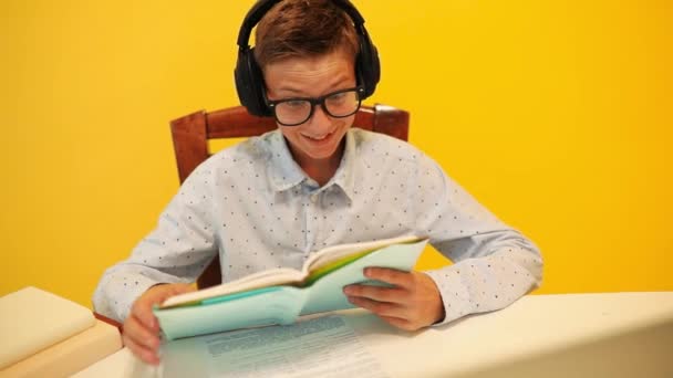 Happy teen guy in headphones using a laptop computer, learning through an online e-learning system, on a yellow background — Stock Video