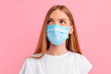 Yüzünde tıbbi koruyucu maske takan, soyutlanmış pembe arka planda düşünceli genç bir kadın. Koronavirüs salgını, karantina, virüs koruması