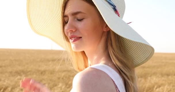 Hermosa chica feliz en un sombrero de paja, en un campo de trigo al atardecer — Vídeos de Stock