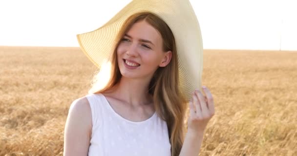 Hermosa chica feliz en un sombrero de paja, en un campo de trigo al atardecer — Vídeos de Stock