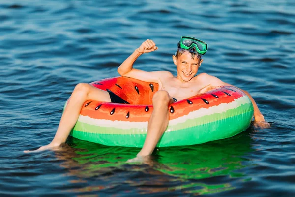 在一个充气圆圈上的男孩在海里游泳 并表现出一种胜利的姿态 一个小男孩玩得很开心 在一个充气的圆圈上游泳 — 图库照片