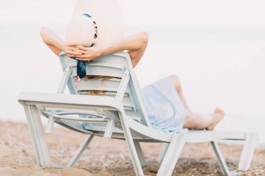 Yaz şapkalı, kumlu bir plajda dinlenen kız şezlongda uzanıyor. Yaz tatili, seyahat.