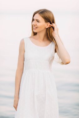 Beyaz bir yaz elbisesi içinde, plajda poz veren güzel bir kızın portresi. Yaz tatili