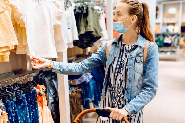 Mladá Žena Kočárkem Obličeji Maskou Lékařské Ochrany Vybírá Dětské Oblečení — Stock fotografie