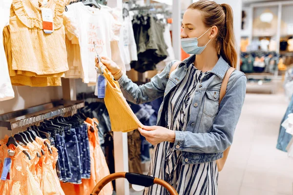 Mladá Žena Kočárkem Obličeji Maskou Lékařské Ochrany Vybírá Dětské Oblečení — Stock fotografie