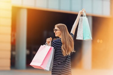 Geriye bakış, güneş gözlüklü mutlu, çekici genç bir kadın, alışveriş merkezinde alışveriş torbaları. moda