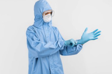 Doktor, covid-2019 koronavirüs salgınıyla savaşmak için koruyucu kıyafet giyiyor. Koruyucu giysi, güvenlik gözlükleri, eldivenler, solunum cihazı, beyaz arka planda.