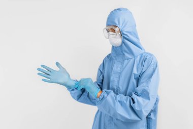 Doktor, covid-2019 koronavirüs salgınıyla savaşmak için koruyucu kıyafet giyiyor. Koruyucu giysi, güvenlik gözlükleri, eldivenler, solunum cihazı, beyaz arka planda.