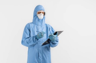 Koronavirüs, gözlük, maske ve eldivenlere karşı koruyucu giysi giyen erkek doktor, izole edilmiş beyaz bir arkaplan üzerine belgeler yazıyor. Coronavirus, covid 19, tıp, sağlık konsepti