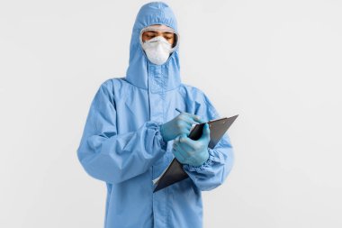 Koronavirüs, gözlük, maske ve eldivenlere karşı koruyucu giysi giyen erkek doktor, izole edilmiş beyaz bir arkaplan üzerine belgeler yazıyor. Coronavirus, covid 19, tıp, sağlık konsepti