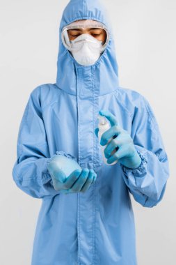 Koronavirüse karşı koruyucu giysi giyen erkek doktor, tıbbi maske, lateks eldiven ve gözlük izole edilmiş beyaz arka planda antiseptik ile ellerini dezenfekte ediyor. Coronavirus, karantina