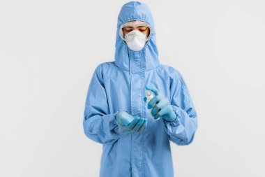 Koronavirüse karşı koruyucu giysi giyen erkek doktor, tıbbi maske, lateks eldiven ve gözlük izole edilmiş beyaz arka planda antiseptik ile ellerini dezenfekte ediyor. Coronavirus, karantina