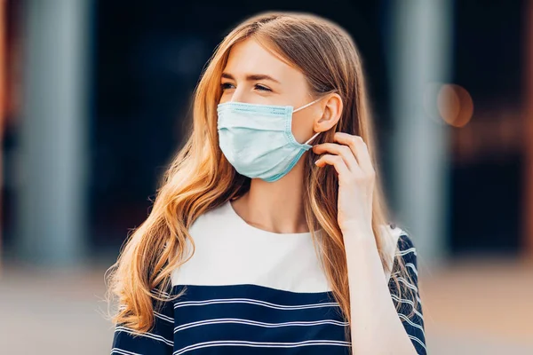 建物を背景に市内に立つ顔の医療保護マスクの魅力的な若い女性 隔離コロナウイルス — ストック写真