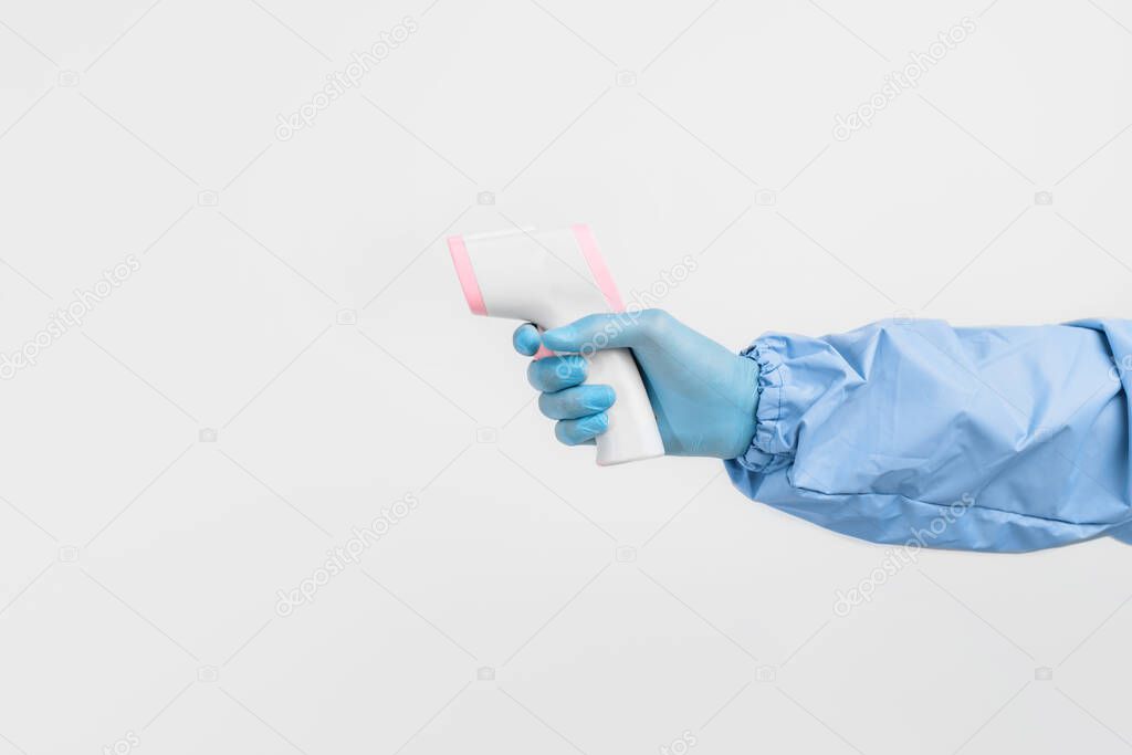 Close-up of a doctor's hand, in a protective suit and gloves, measuring the temperature with an infrared non-contact thermometer on an isolated white background. Coronavirus, quarantine
