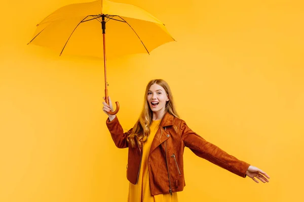 Happy emotional girl in a yellow dress and autumn jacket, laughing and having fun with a yellow umbrella on an yellow background