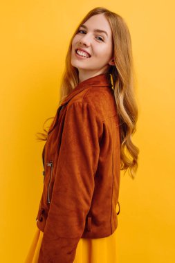 Parlak sarı elbiseli ve sonbahar ceketli, güzel, çekici, mutlu bir kız, izole edilmiş sarı bir arka planda poz veriyor. Sonbahar konsepti