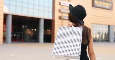  Yüzünde tıbbi koruyucu maske takan, siyah bir elbise ve şapkayla alışveriş merkezinde alışveriş yapan alışveriş manyağı bir kız. Kara Cuma, alışveriş.