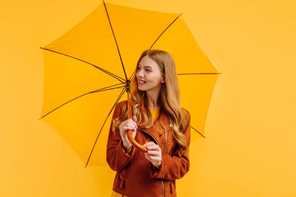 happy girl, in a bright yellow dress and an autumn jacket, stands with a yellow umbrella on a yellow background