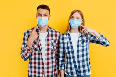 Virüslere karşı korunmak için tişört ve tıbbi maske takan erkek ve kadın izole edilmiş sarı bir arka planda duruyorlar.