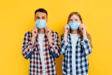 Virüslere karşı korunmak için tişört ve tıbbi maske takan erkek ve kadın izole edilmiş sarı bir arka planda duruyorlar.