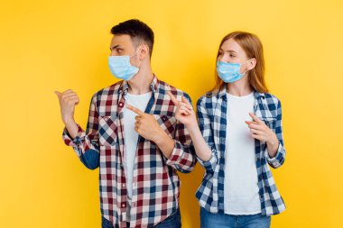 Yüzlerinde tıbbi koruyucu maskeler ve gömlekli bir adam ve bir kadın izole edilmiş sarı arka plandaki boşluğun bir kopyasını gösteriyorlar.