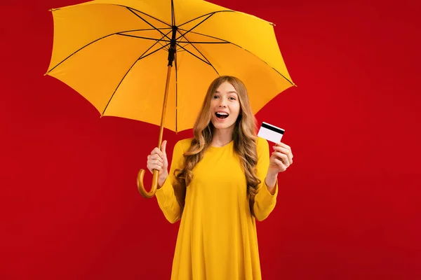 一个带着雨伞和信用卡的快乐的年轻女人 带着红色背景和购物的概念 吓了一大跳 — 图库照片