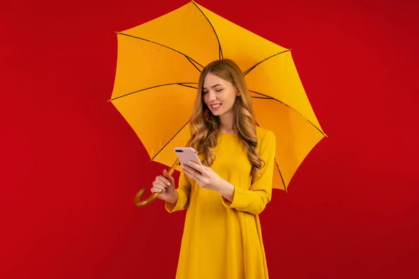 Gyönyörű Fiatal Sárga Ruha Esernyő Segítségével Mobiltelefon Piros Háttér — Stock Fotó