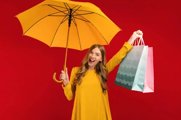 黄色の傘と赤い背景のショッピングバッグを持つ刺激的な揺れ若い女性 — ストック写真