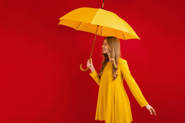 happy young woman with yellow umbrella on red background, autumn concept