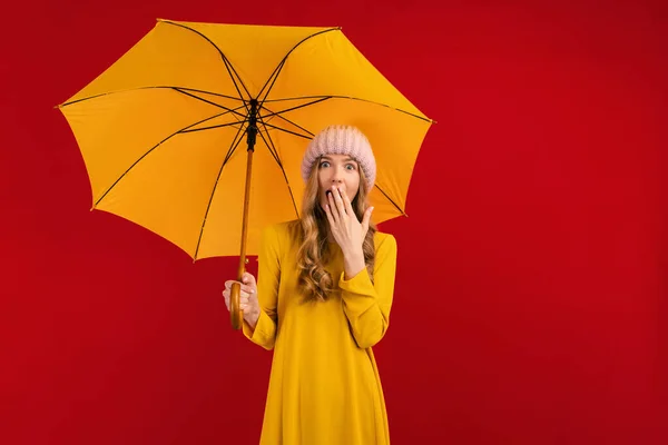 Потрясенная Красивая Молодая Женщина Зонтиком Теплой Шляпе Голове Красном Фоне — стоковое фото