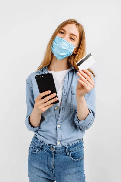 Boldog Fiatal Orvosi Maszkban Arcán Műanyag Hitelkártyával Mobiltelefonnal Fehér Alapon — Stock Fotó