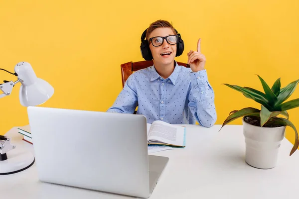 Home schooling and distance education for children. thoughtful smart student sitting at the table, learning by video link with the teacher, on a yellow background