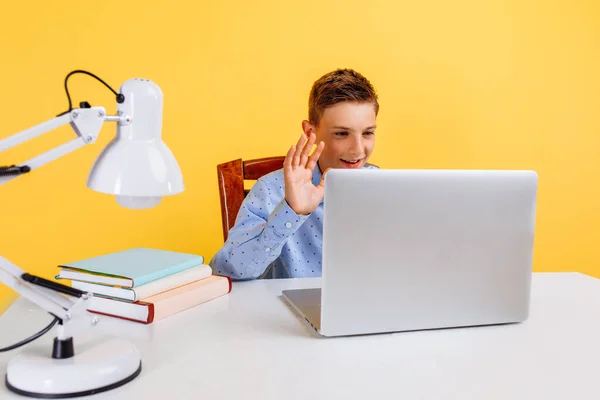 Çocuklar için online dersler. Çocuklar için evde eğitim ve uzak eğitim. Okul çocuğu masada oturuyor, öğretmeniyle video bağlantısı kurarak öğreniyor, sarı arka planda.
