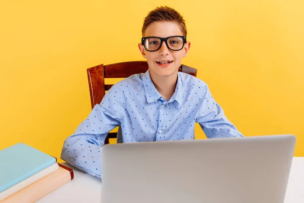 distance education for children. a student is sitting at a table, studying by video link with a teacher, on a yellow background