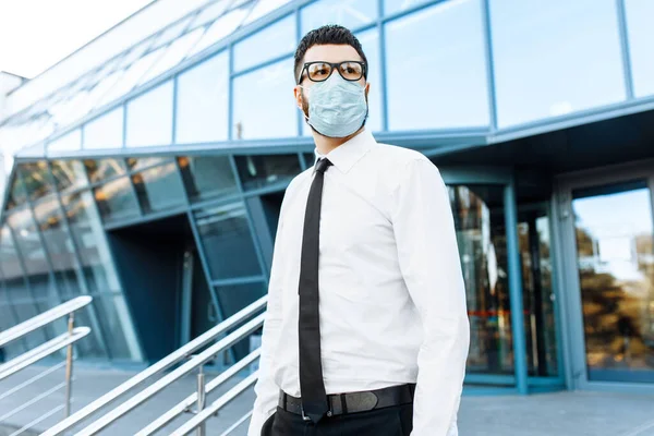 Man businessman in business clothes and a medical protective mask on his face, against the background of a glass office building