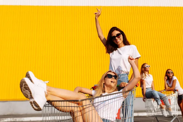 2人の美しい幸せな若い女性 白いTシャツのガールフレンドは 夏の晴れた日にショッピングセンターの背景にあるショッピングカートで楽しいです — ストック写真