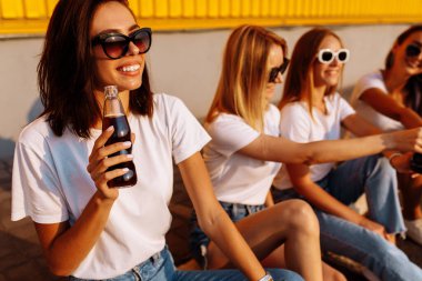 Genç ve mutlu arkadaşlar, güneşli bir yaz gününde birlikte içki içip eğlenirler. Sarı bir duvarın arkasında. Dostluk ve kutlama kavramı..