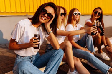 Genç ve mutlu arkadaşlar, güneşli bir yaz gününde birlikte içki içip eğlenirler. Sarı bir duvarın arkasında. Dostluk ve kutlama kavramı..