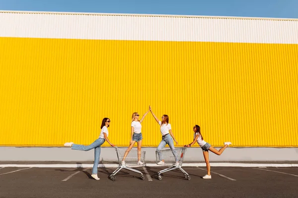 一群快乐的年轻人在购物车上玩乐 在一个阳光明媚的夏天 年轻美丽的姑娘们在购物中心的一面黄色的墙的后面赶着马车 — 图库照片
